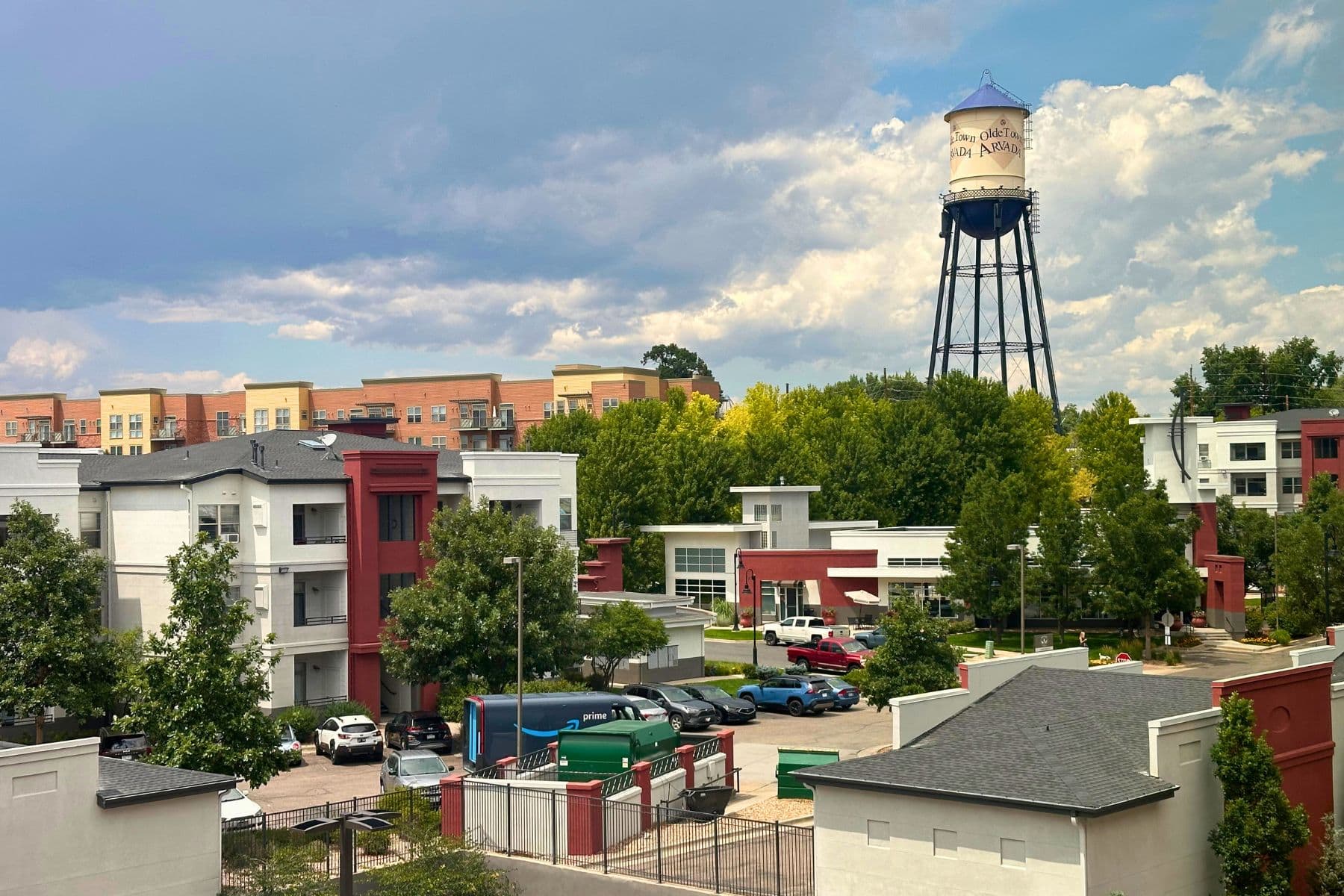 Olde Town Arvada water tower overlooking modern apartment buildings and tree-lined streets under a partly cloudy sky